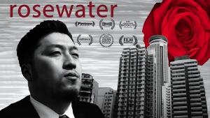 A black and white composite image of a young Japanese man’s face in three-quarter profile. He has short hair and light facial hair and is wearing a suit. Behind him are tall buildings against a gray static background. A bright red rose hovers behind the buildings like the sun.